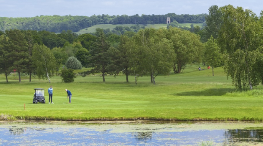 Belton Woods Golf Club, Lincolnshire - golf course view from across lake, with 2 players at the tee in the distance