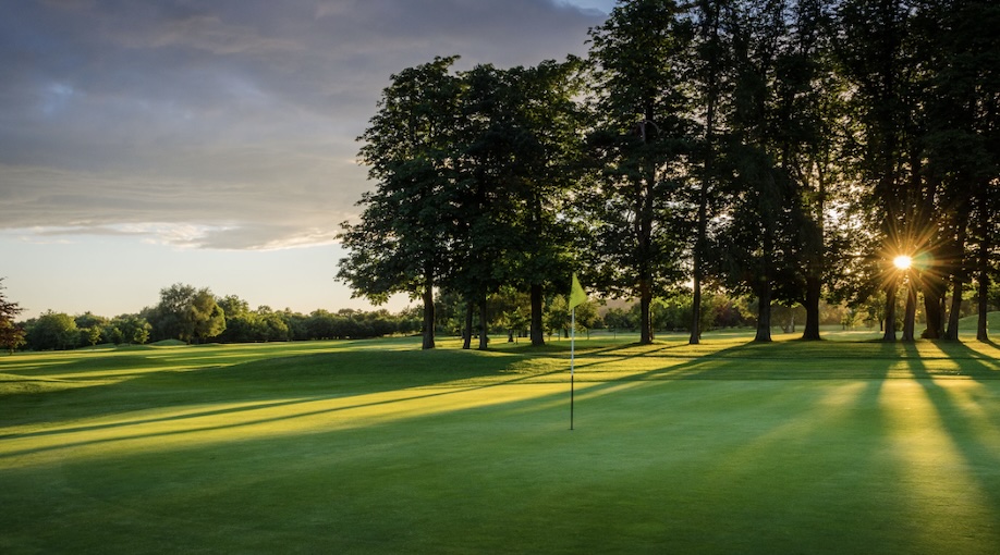 Drift Golf Club, Surrey, - View of golf course on green with flag hole, fairway and sunsetting through trees