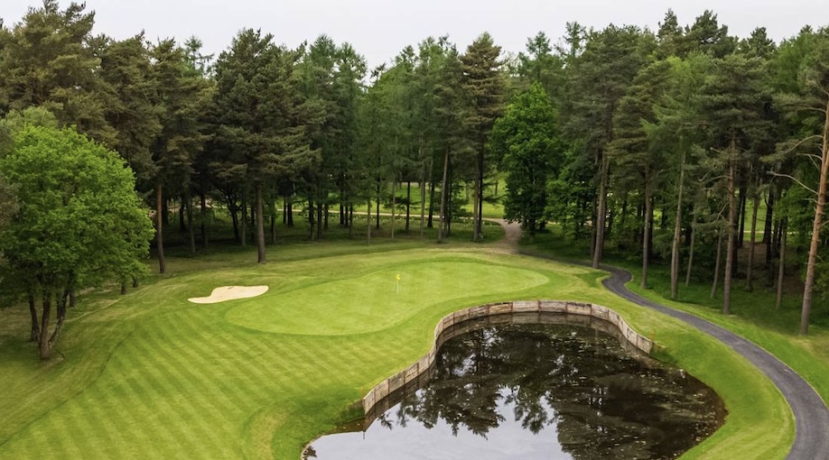 Foxhills Golf Club, Surrey - Aerial view of golf course green with small bunker, large pond water feature and trees