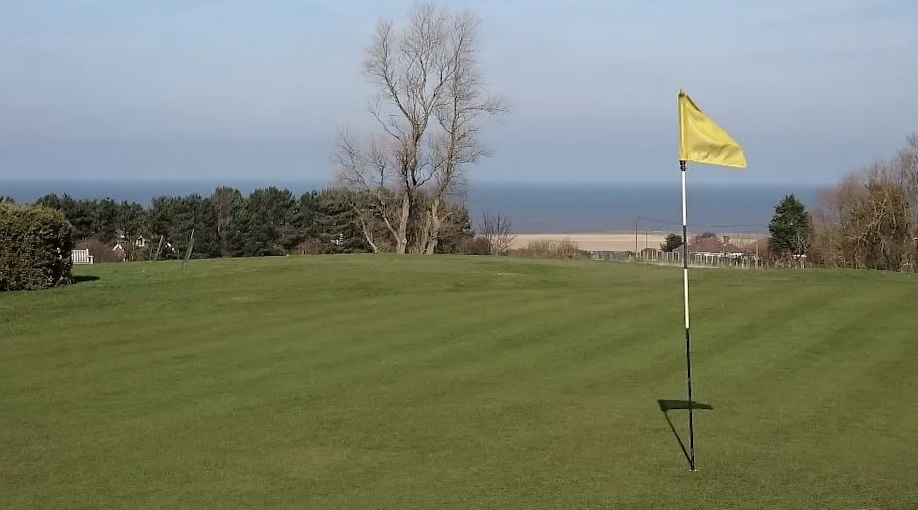 The Links Hotel & Golf Club, Norfolk- Golf course view on green with flag and coastline in the distance